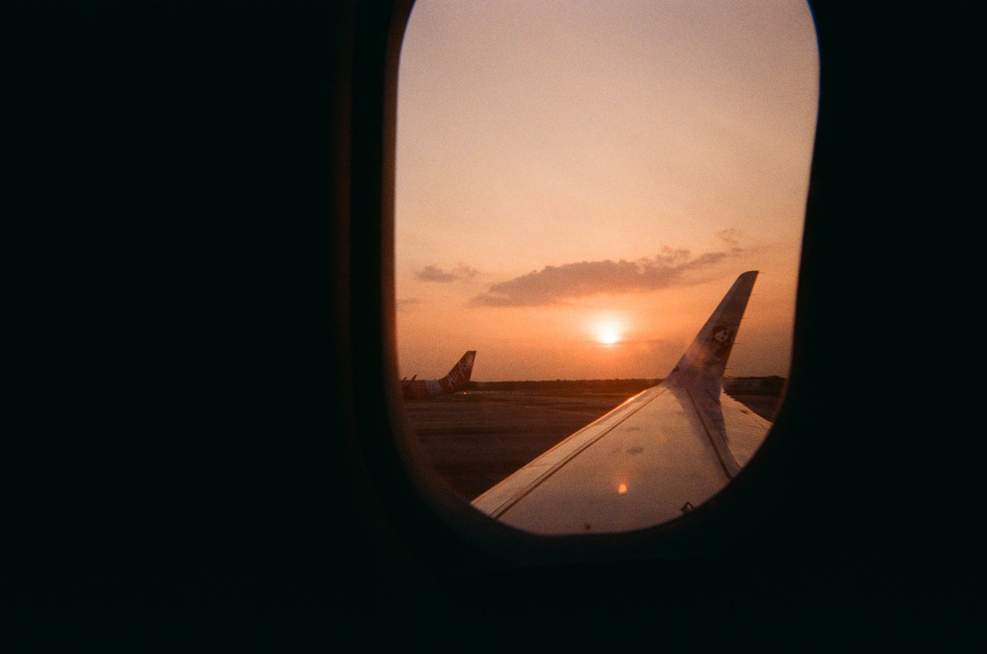 Sunset through a plane window, over the wing and the runway